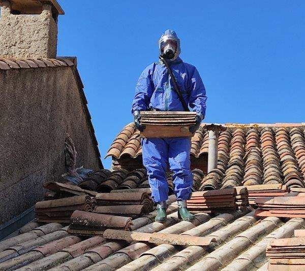 Intervenant en combinaison et masque de protection sur une toiture en tuiles