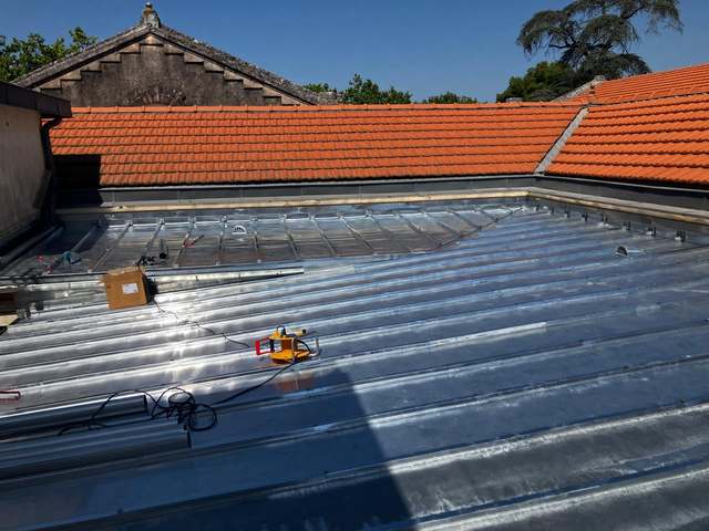 Toiture en zinc en cours de pose entre deux pans de tuiles